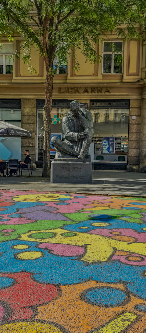 A statue of Nikola Tesla with a vibrant cat mural at his feet.