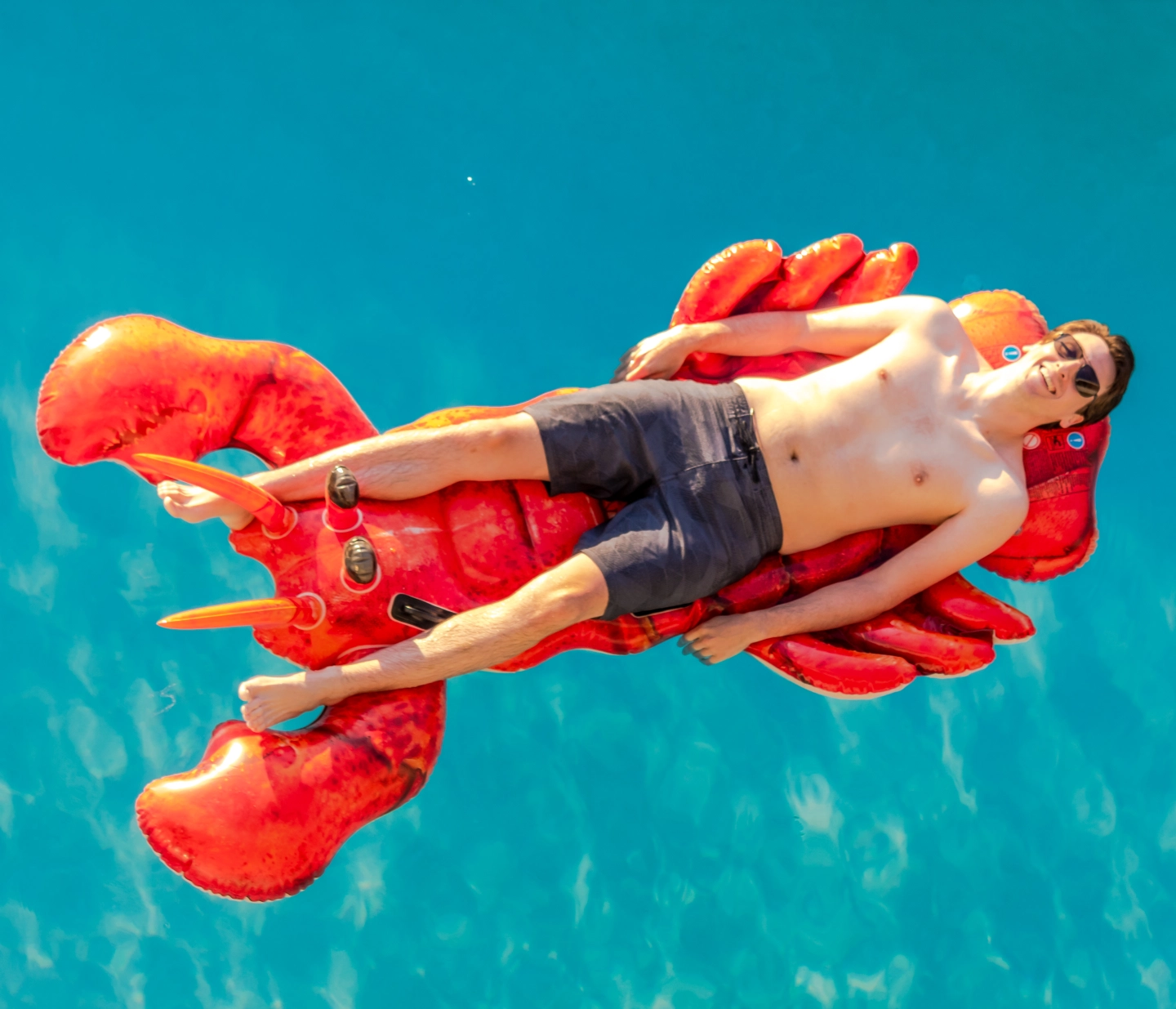 A man laughing while floating in the pool on a lobster pool float