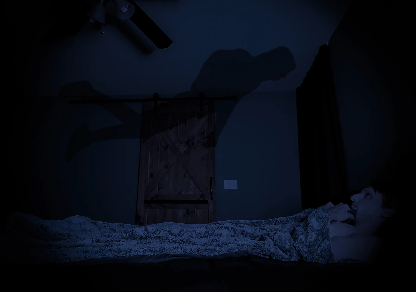 A man laying in bed clutching his blanket to his chin, while looking up at the figure floating above his bed staring back at him